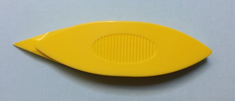 Op de afbeelding: Een gele plastic garennaald met een puntige punt en een getextureerd ovaalvormig handvat.
