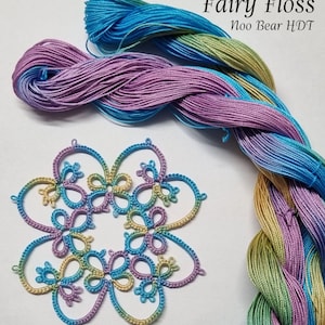 Puede incluir: Primer plano de un encaje de ganchillo de colores con un diseño floral. El encaje está hecho con un hilo degradado de azul, verde y morado. El hilo también se muestra en ovillos, etiquetados como "Fairy Floss Noo Bear HDT".