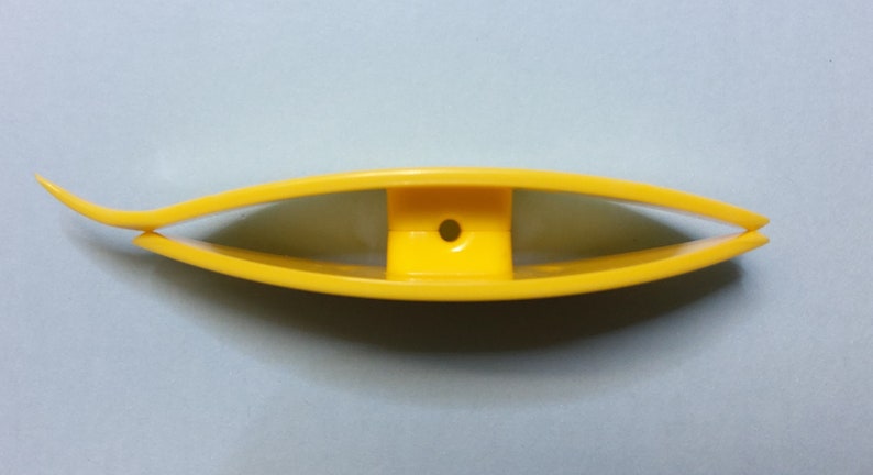 Op de afbeelding: Een geel plastic gereedschap met een gebogen handvat en een klein gaatje in het midden. Het gereedschap is bedoeld om te helpen met naaien of knutselen.