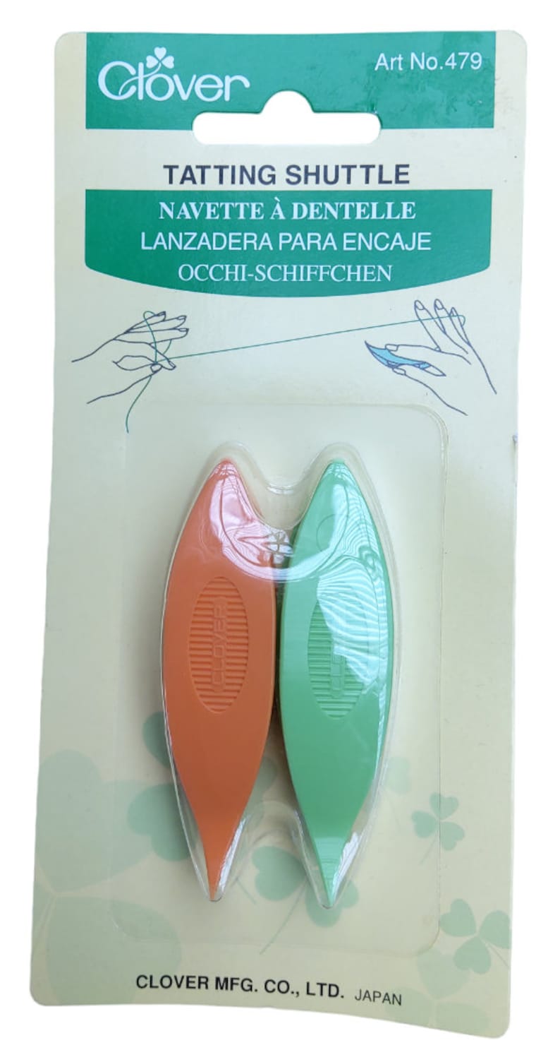 Op de afbeelding: Twee plastic tatting shuttles, &eacute;&eacute;n oranje en &eacute;&eacute;n groen, verpakt op een witte en groene achtergrond. De verpakking bevat de tekst "Clover Tatting Shuttle" en "Art No. 479".