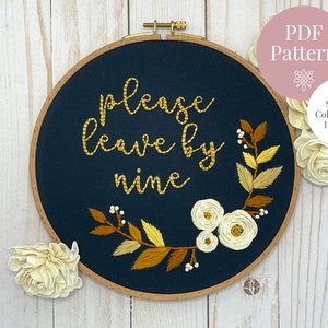 May include: Embroidered hoop art with the text "Please leave by nine" in gold thread. The hoop is navy blue and features a floral design with white and gold flowers and leaves.