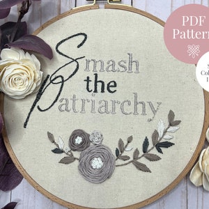 May include: Embroidered hoop art with the text "Smash the Patriarchy" in black cursive lettering. The hoop is decorated with a floral design in shades of gray and brown.
