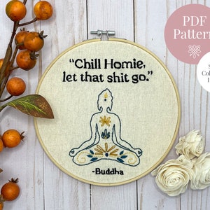 May include: Embroidered hoop art with a quote from Buddha: "Chill Homie, let that shit go." The embroidery features a stylized image of a meditating Buddha in blue and yellow thread on a beige fabric background.