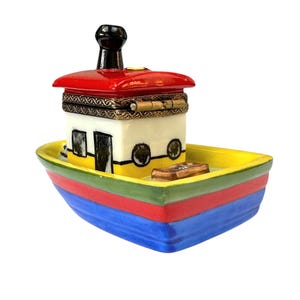 Puede incluir: Una caja de baratijas decorativa con forma de barco colorido. El barco tiene una parte superior roja, una cabina blanca y amarilla con detalles negros y un casco multicolor. Una chimenea negra se eleva desde la parte superior.
