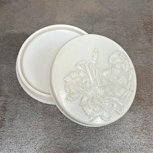 Può includere: Una scatola portaoggetti in ceramica bianca con un design floreale sul coperchio. Il coperchio è aperto e l'interno della scatola è visibile.