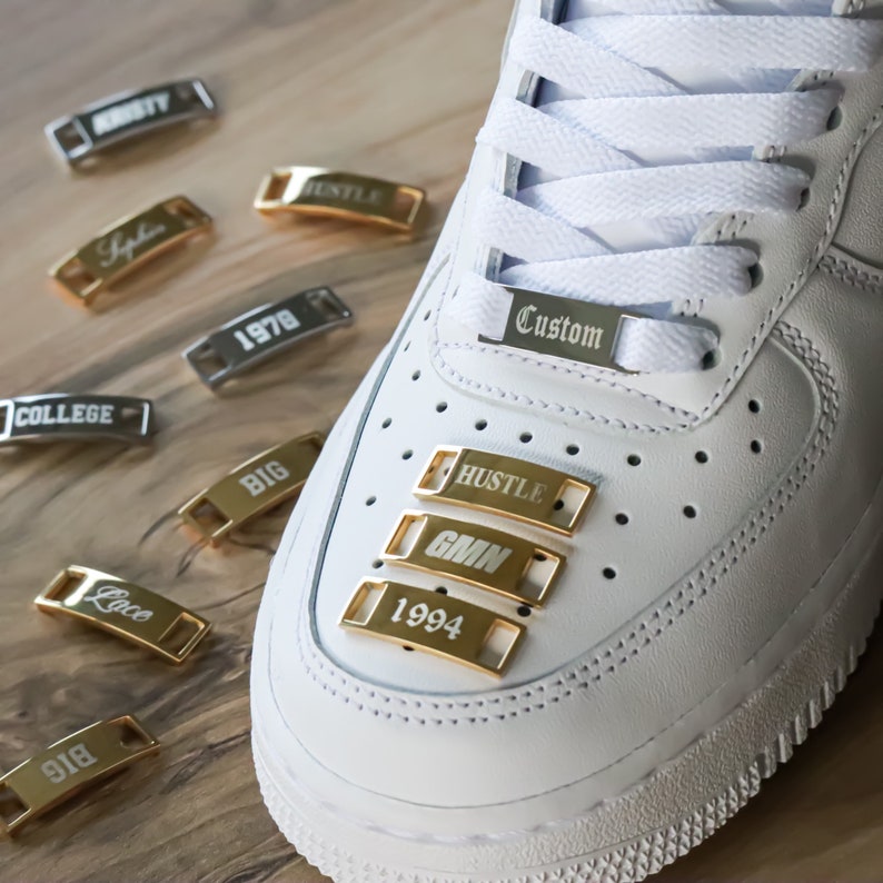 May include: White sneakers with gold shoe charms that say "Hustle", "GMN", "1994", and "Custom".