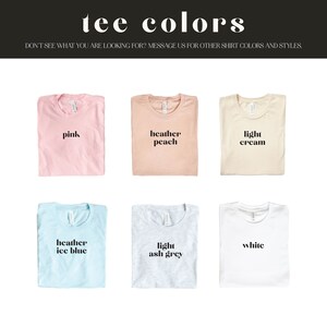 May include: Six folded t-shirts in different colors, including pink, peach, cream, light blue, light gray, and white. Each shirt has a different color name printed on it in black text.