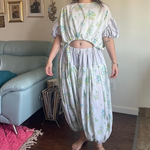 May include: A two-piece outfit consisting of a cropped top and matching harem-style pants. The fabric is white with a blue and green floral print, accented by black and white polka dot and striped panels on the sleeves and waistband.