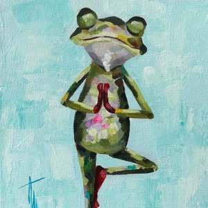 May include: A green frog with pink accents is standing on one leg in a yoga pose with its hands in a prayer position. The frog is on a blue and green surface with a light blue background.