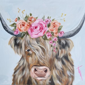 May include: A brown and white Highland cow with long, shaggy hair wears a crown of pink and orange flowers. The cow has a pink nose and is looking directly at the viewer.