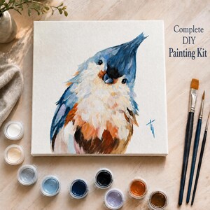 May include: A square canvas featuring an oil painting of a tufted titmouse with blue, white, and brown feathers. The text Complete DIY Painting Kit is printed in the upper right corner. Includes three paintbrushes and ten small paint pots.