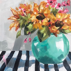 May include: A teal blue vase with a round body holds a bouquet of orange and yellow sunflowers with pink flowers. The vase is sitting on a black and white striped surface.
