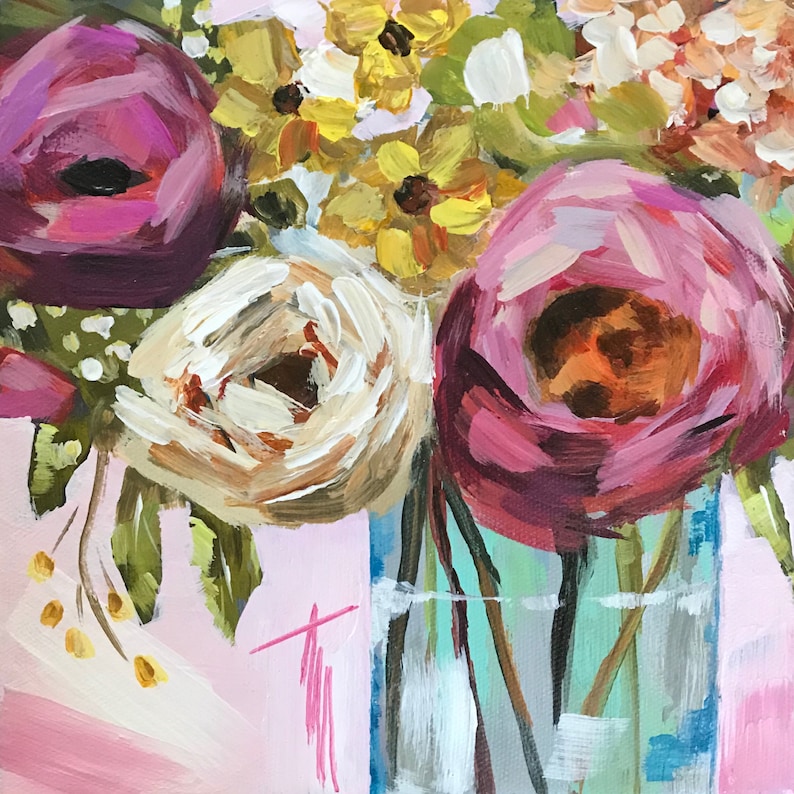 May include: A bouquet of pink, white, and yellow flowers in a clear glass vase. The flowers are arranged in a loose, natural style. The vase is sitting on a pink surface.