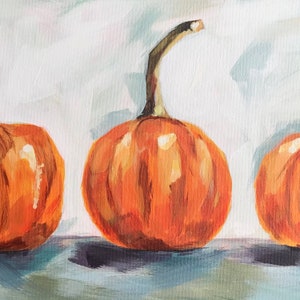 May include: Three orange pumpkins with stems, painted in a realistic style on a light blue background.