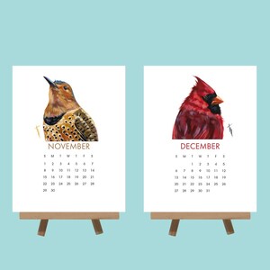 May include: Two small wooden easels display calendar pages. One shows a woodpecker illustration with "NOVEMBER", the other a red cardinal with "DECEMBER". Each calendar has a monthly grid.