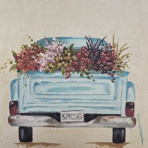 May include: A light blue vintage pickup truck with a bed full of colorful flowers. The truck has a license plate that reads "SPRING".