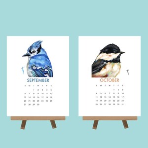 May include: Two small wooden easels each hold a calendar page. One features a blue jay and the word "SEPTEMBER". The other shows a black-capped chickadee and the word "OCTOBER". Each calendar has a month grid.