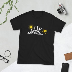 May include: Black t-shirt with a white graphic of the evolution of skiing. The graphic shows a stick figure evolving from a caveman to a skier. The graphic also includes a yellow sun and a mountain.