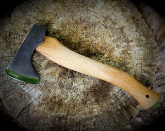 May include: A black axe with a wooden handle. The axe head has a green epoxy finish. The axe is resting on a tree stump.
