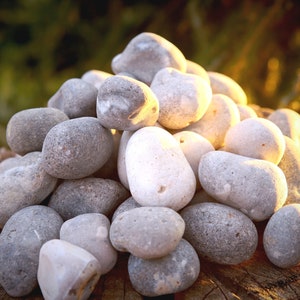 Könnte beinhalten: Ein Haufen glatter, grauer und weißer Steine, die auf einer Holzoberfläche in Pyramidenform angeordnet sind. Die Steine sind in verschiedenen Größen und Formen, wobei einige eine abgerundetere Form haben als andere.