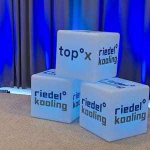 May include: Three white cube-shaped stools with the text "top° x riedel° kooling" on the top stool and "riedel° kooling" on the other two stools.