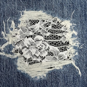 Peut inclure: Gros plan sur un trou dans un jean bleu, avec de la dentelle blanche qui apparaît à travers la déchirure.