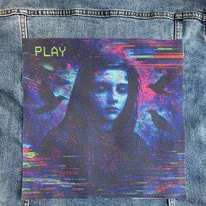 Puede incluir: Chaqueta vaquera azul claro con un parche colorido que presenta un retrato de una persona con pájaros y la palabra "PLAY". El parche tiene un estilo de arte glitch con tonos azules, morados y rojos.