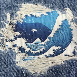 May include: A blue and white wave design is patched onto a ripped pair of denim jeans. The wave design is reminiscent of a traditional Japanese woodblock print.