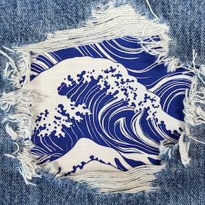 Op de afbeelding: Een blauw en wit golfpatroon is zichtbaar door een gescheurd gat in een blauwe spijkerbroek.