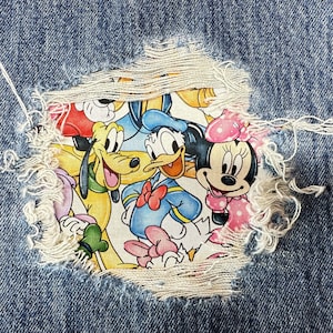 Könnte beinhalten: Ein Jeans-Patch mit einem bunten Cartoon-Bild von Mickey Mouse, Minnie Mouse, Donald Duck, Goofy und Pluto. Die Figuren lächeln und winken.