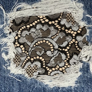 May include: A close-up of a denim fabric with a hole that has been patched with black and white lace.