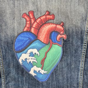Op de afbeelding: Een geborduurd hart met een golfpatroon in rood, blauw en groen, genaaid op een spijkerjack.