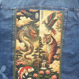 Op de afbeelding: Blauwe spijkerjas met een grote, kleurrijke afbeelding op de rug met een draak, feniks, tijger en koi-vis in een traditionele Aziatische kunststijl. Het kunstwerk bevat wolken, watervallen en bloemelementen.