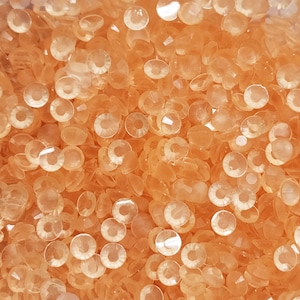 May include: A close-up image of a large quantity of small, translucent, peach-colored, round, flat, decorative sequins.