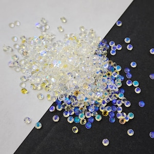 May include: A large pile of iridescent clear and blue rhinestones. The rhinestones are scattered on a white and black surface.