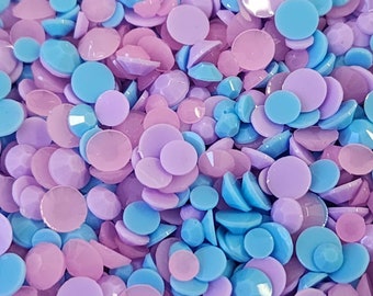 May include: A close-up of a pile of small, round, iridescent rhinestones in shades of light blue and lavender.