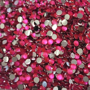 May include: A large pile of small, round, pink and silver rhinestones. The rhinestones have a flat back and a faceted front.