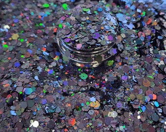 May include: A close-up of iridescent glitter in shades of black, blue, green, and purple. The glitter is in a small jar and is perfect for crafting or decorating.