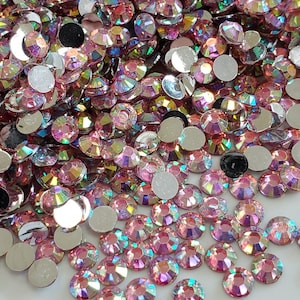 Könnte beinhalten: Eine große Menge an schimmernden rosa Strasssteinen, auch bekannt als Kristalle oder Edelsteine, sind auf einer weißen Oberfläche verstreut. Die Strasssteine haben ein facettiertes Design und sind perfekt zum Basteln und für die Schmuckherstellung.