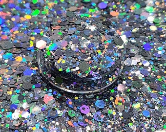 May include: A close-up of a container filled with black glitter. The glitter particles are various shapes and sizes, including hexagons. The glitter has a holographic effect, reflecting multiple colors including green, blue, and purple.