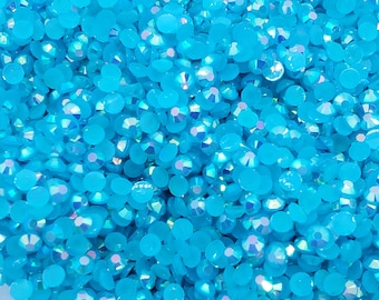 May include: A close-up image of a large quantity of turquoise blue iridescent rhinestones. The rhinestones are scattered and overlapping, creating a shimmering effect.