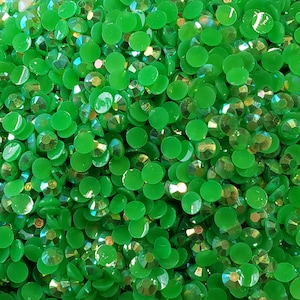 May include: A close-up image of a large quantity of small, round, green rhinestones. The rhinestones have a slightly iridescent finish.