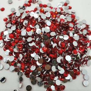 Könnte beinhalten: Eine große Menge an roten und silbernen runden Strasssteinen. Die Strasssteine sind auf einer weißen Oberfläche verstreut.