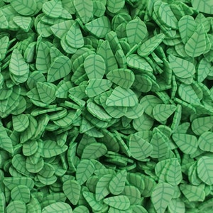 May include: A large pile of green leaf-shaped sprinkles. The sprinkles are made of a smooth, pliable material and have a raised vein pattern.