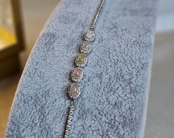 Op de afbeelding: Een zilveren armband met een delicate ketting en vijf ovale opalen die in zilver zijn gezet. De opalen zijn iriserend en hebben een regenboog aan kleuren.