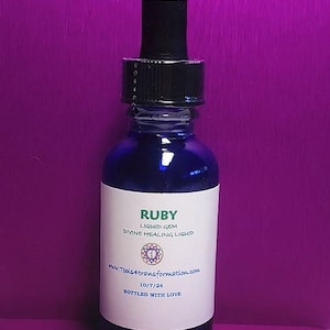 Puede incluir: Una pequeña botella de vidrio azul con un gotero negro. La etiqueta dice "RUBY LIQUID GEM DIVINE HEALING LIQUID www.tools4transformation.com 10/7/24 BOTTLED WITH LOVE."