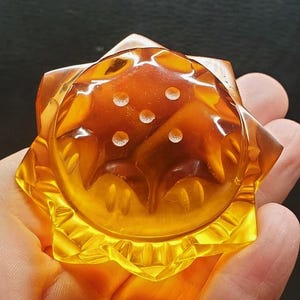 May include: A translucent amber-coloured glass object with a star-shaped base and a rounded top. The surface features five small, circular indentations arranged in a pentagonal pattern on the upper dome, with faceted edges along the perimeter.