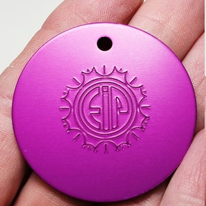 May include: A round, purple metal tag with a hole at the top. The tag has a sunburst design with the letters "EIP" in the center.