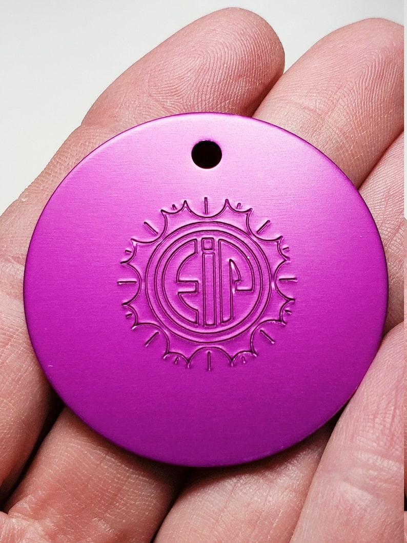 May include: A round, purple metal tag with a hole at the top. The tag has a sunburst design with the letters "EIP" in the center.
