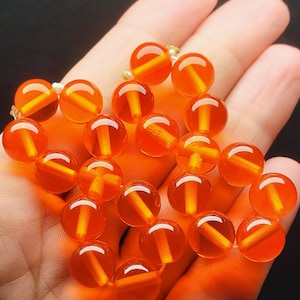 May include: A strand of orange amber beads, each bead is round and translucent with a visible line running through the centre.